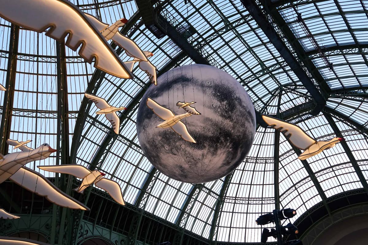 Illuminated paper birds and a monumental moon suspended beneath a glass-and-iron dome