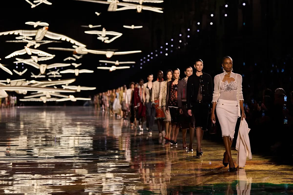 The finale line of models on the mirrored runway beneath a flock of illuminated birds